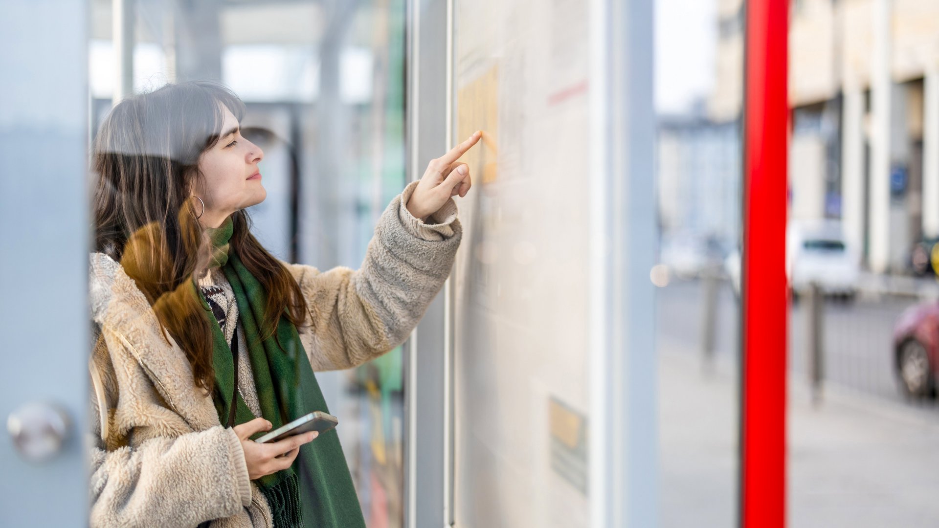 Frau liest Busfahrplan an Haltestelle mit Handy in der Hand Frau liest Busfahrplan an Haltestelle mit Handy in der Hand