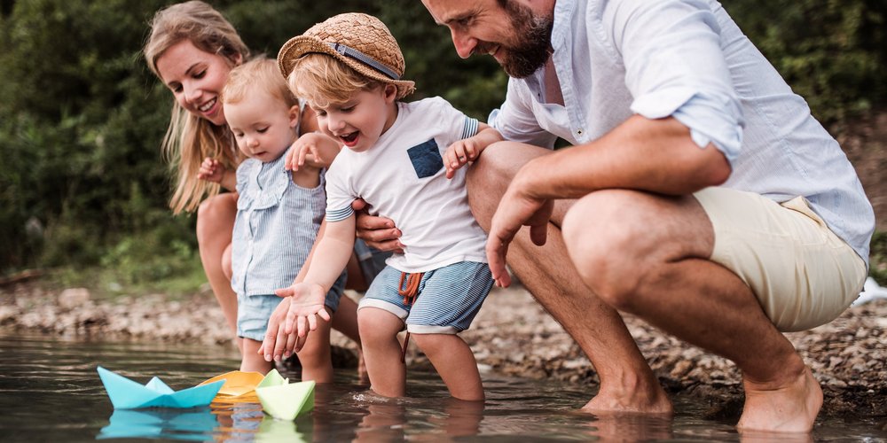 Familie mit Papierschiffchen am Fluss