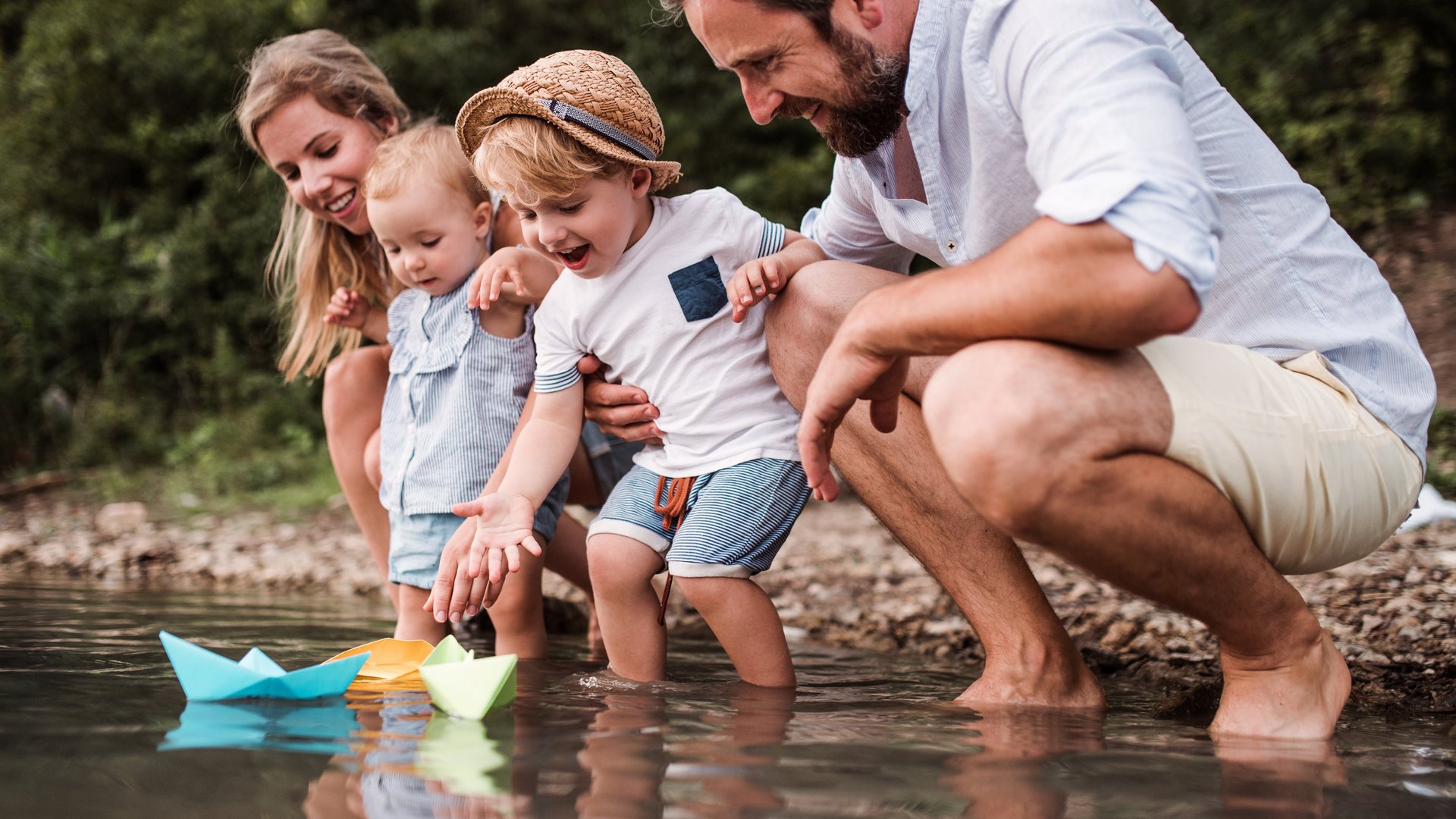 Familie mit Papierschiffchen am Fluss
