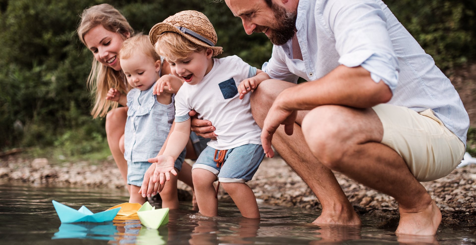 Familie mit Papierschiffchen am Fluss