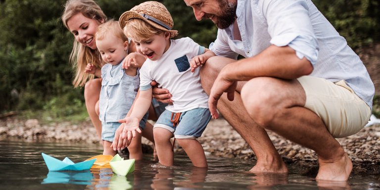 Familie mit Papierschiffchen am Fluss