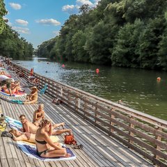 Menschen sonnen sich auf der Holzbank am Hain