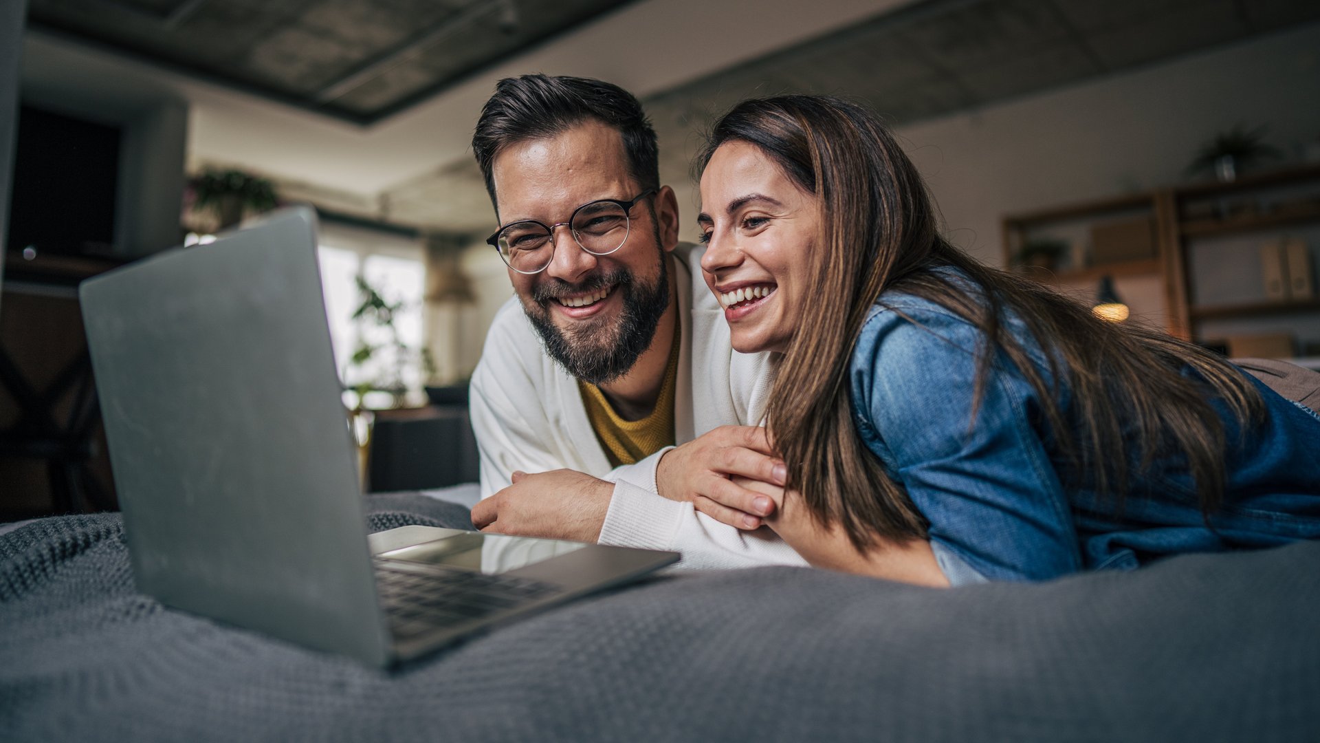 Ein Mann und eine Frau liegen gut gelaunt auf einem Bett und blicken in ein Noteblock