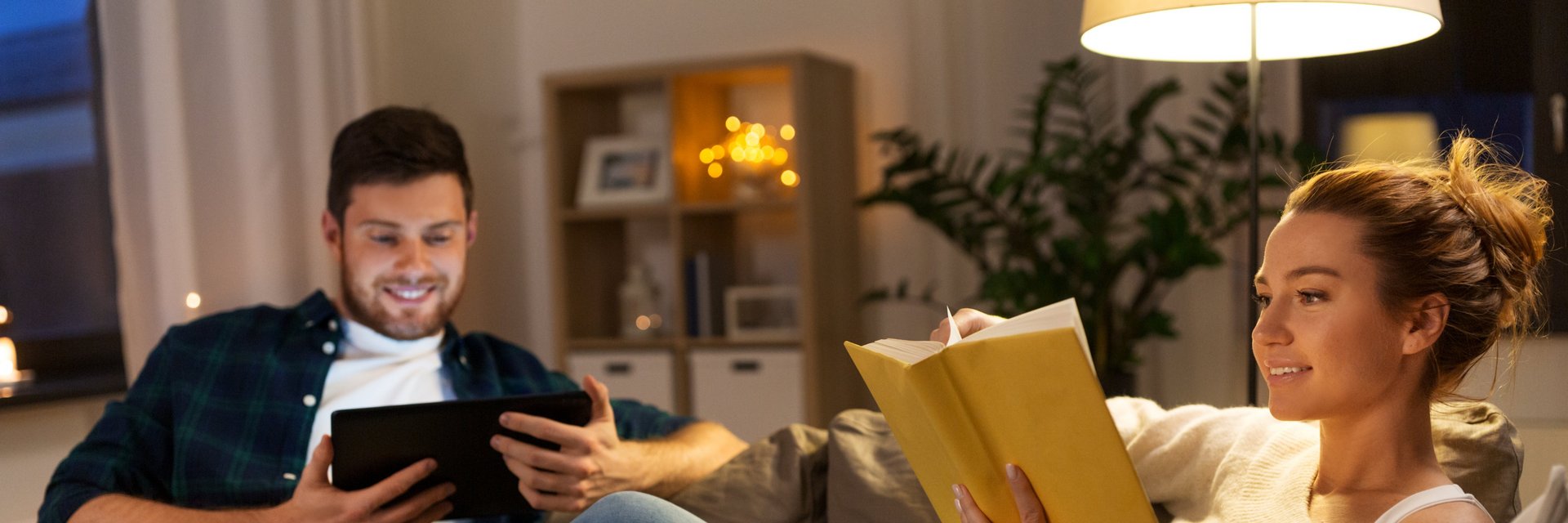 Junger Mann und junge Frau sitze am Sofa und lesen unter Stehlampe