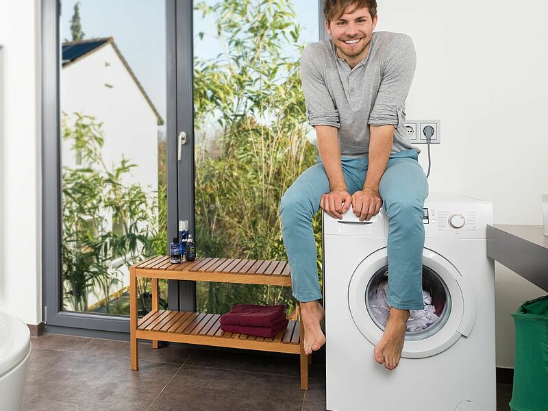 Junger Mann auf Waschmaschine, Symbolbild Stromverbrauch