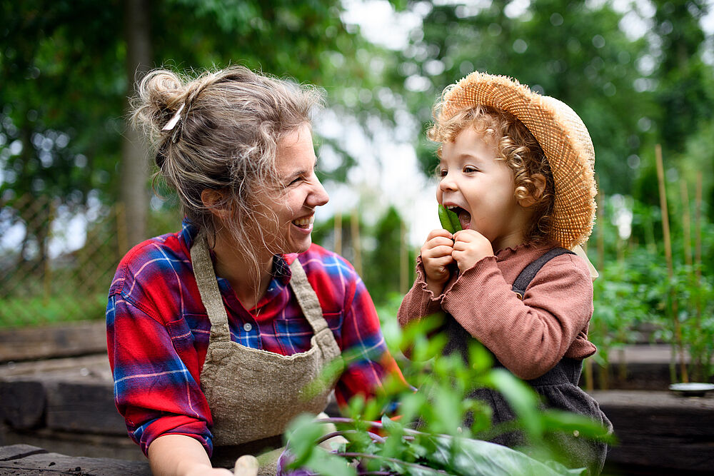 Frau mit Gartenschürze und lachendem Kind im Garten