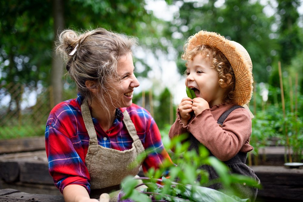 Frau mit Gartenschürze und lachendem Kind im Garten Frau mit Gartenschürze und lachendem Kind im Garten