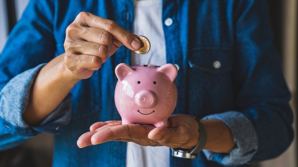 Mann wirft Geld in ein rosa Sparschwein Mann wirft Geld in ein rosa Sparschwein
