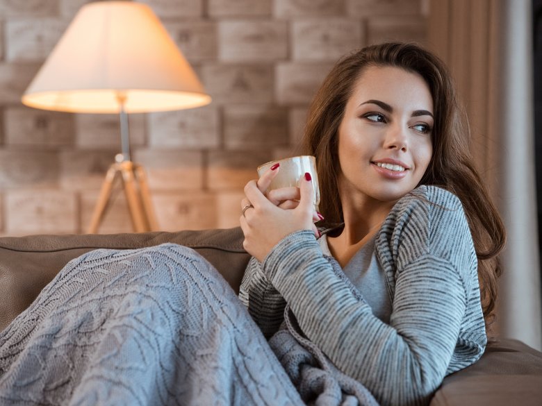 Frau in gemütlicher warmer Wohnung mit einer Teetasse in der Hand