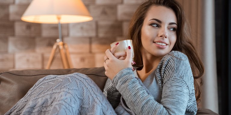 Frau in gemütlicher warmer Wohnung mit einer Teetasse in der Hand