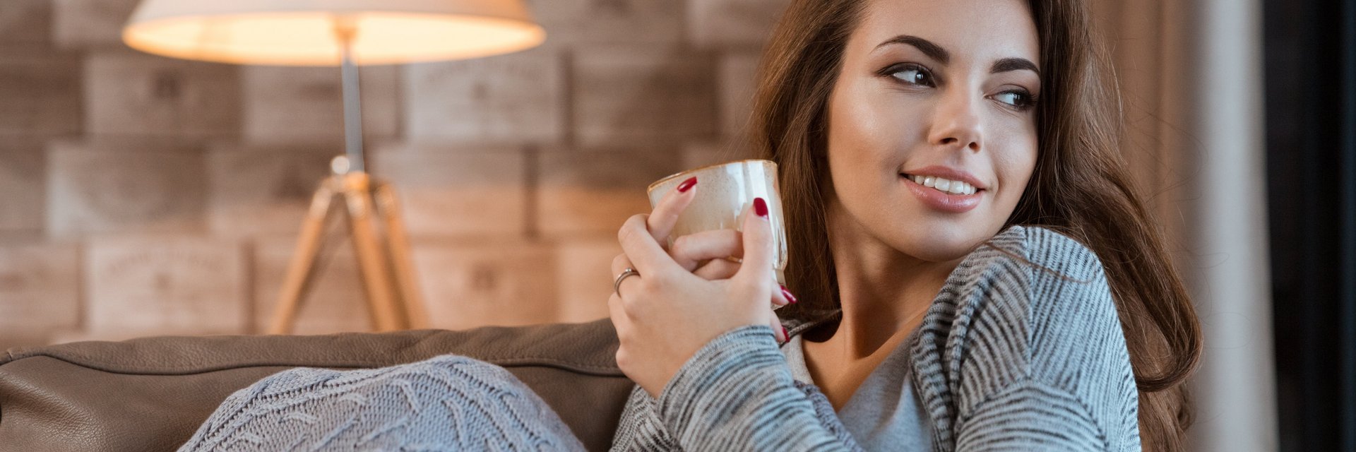 Frau in gemütlicher warmer Wohnung mit einer Teetasse in der Hand