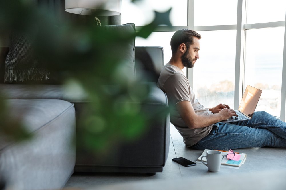 Mann sitzt mit Laptop am Boden Mann sitzt mit Laptop am Boden