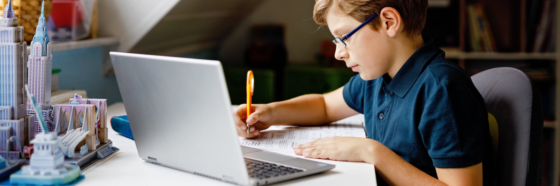 Schüler am Schreibtisch vor einem Laptop macht Hausaufgaben