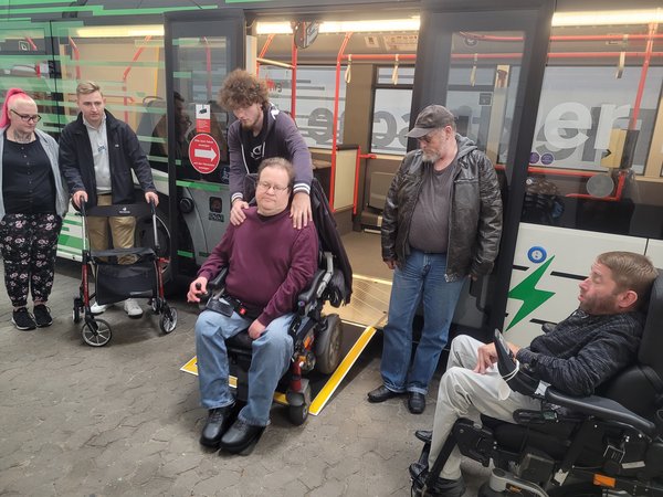 Junger Herr übt, wie er jemandem im Rollstuhl beim Bus verlassen helfen kann