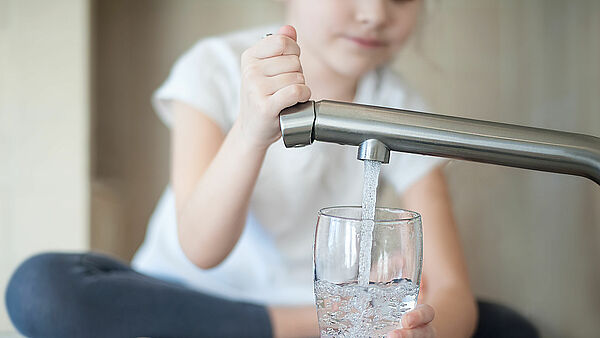 Kind zapft Trinkwasser aus Wasserhahn