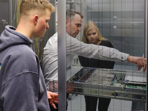 Mann zeigt zwei anderen Personen etwas bei der Technik