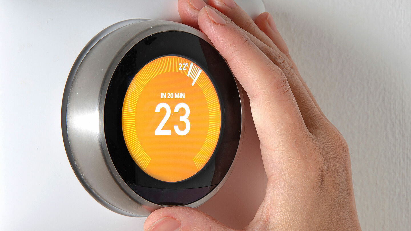 Hand dreht an einem digitalen Thermostat auf 23 Grad Temperatur