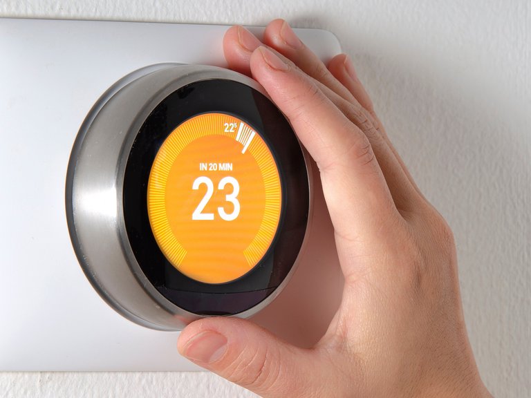 Hand dreht an einem digitalen Thermostat auf 23 Grad