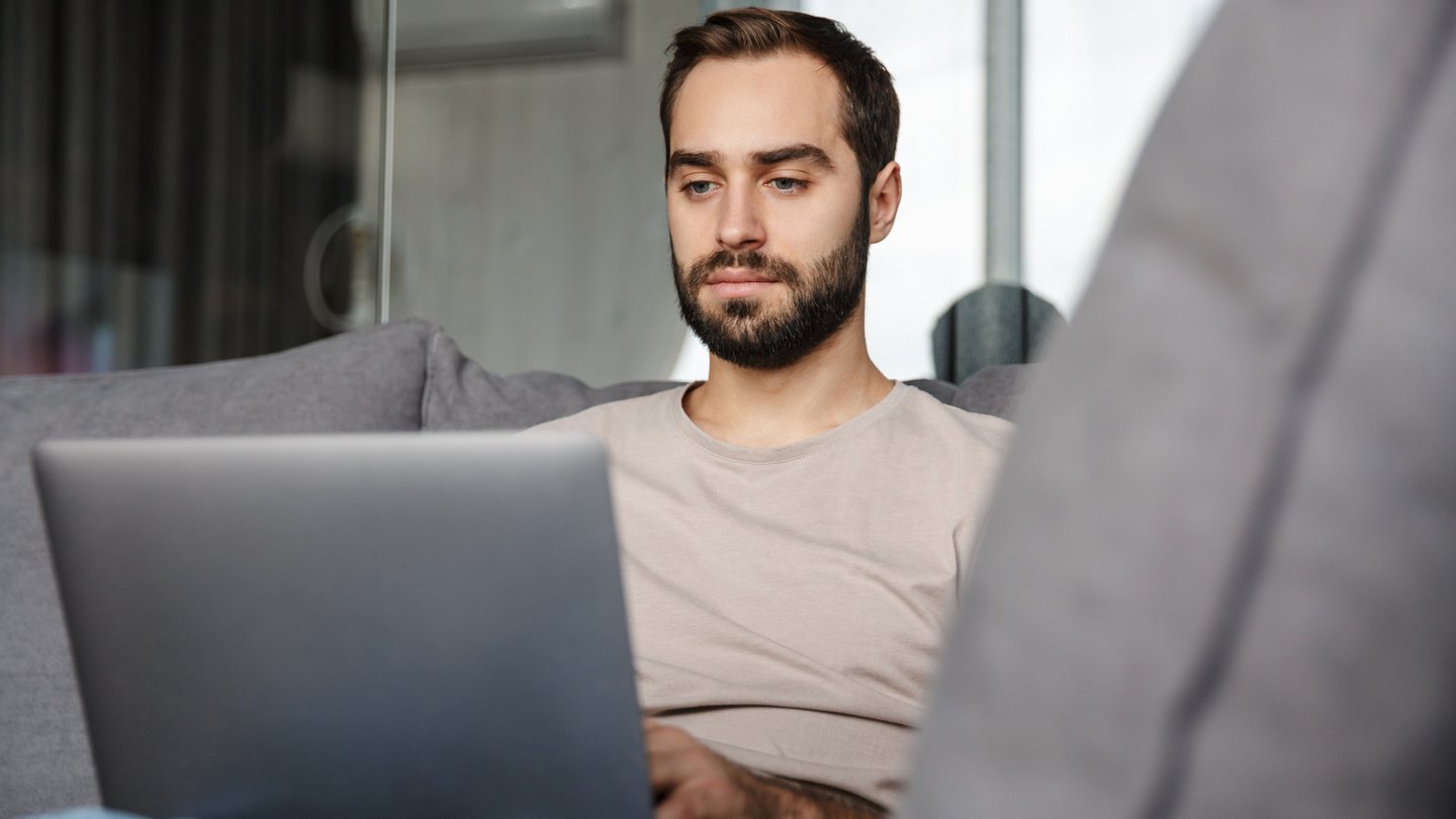 Mann sitzt mit Laptop am Sofa