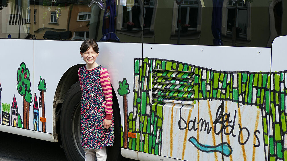 Mädchen steht vor Bus mit selbstgestaltetem Motiv