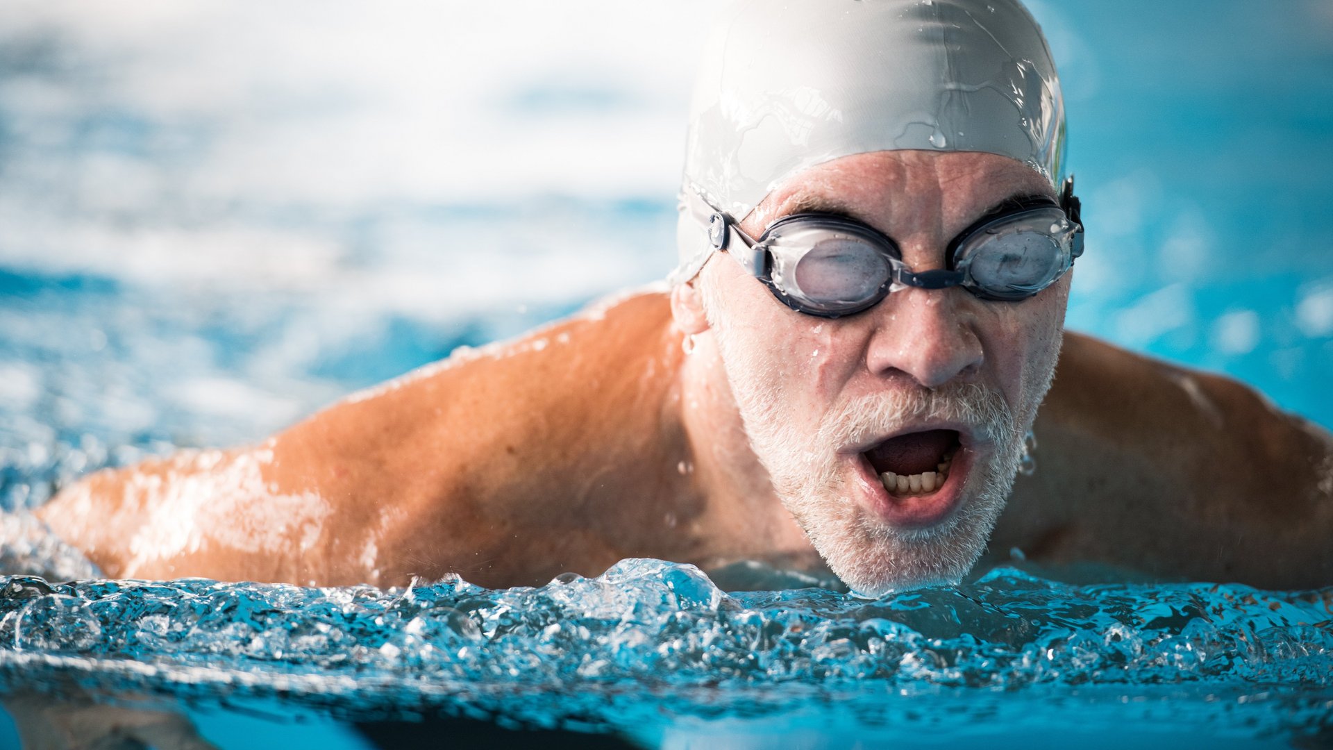 Mann im Seniorenalter schwimmt mit Schwimmbrille und Badekappe