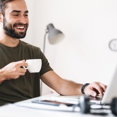 Junger Mann am Laptop und Kaffeetasse in der Hand 