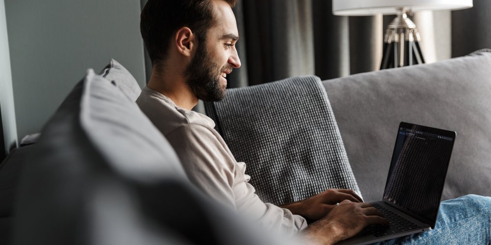 Mann sitzt mit Laptop am Sofa